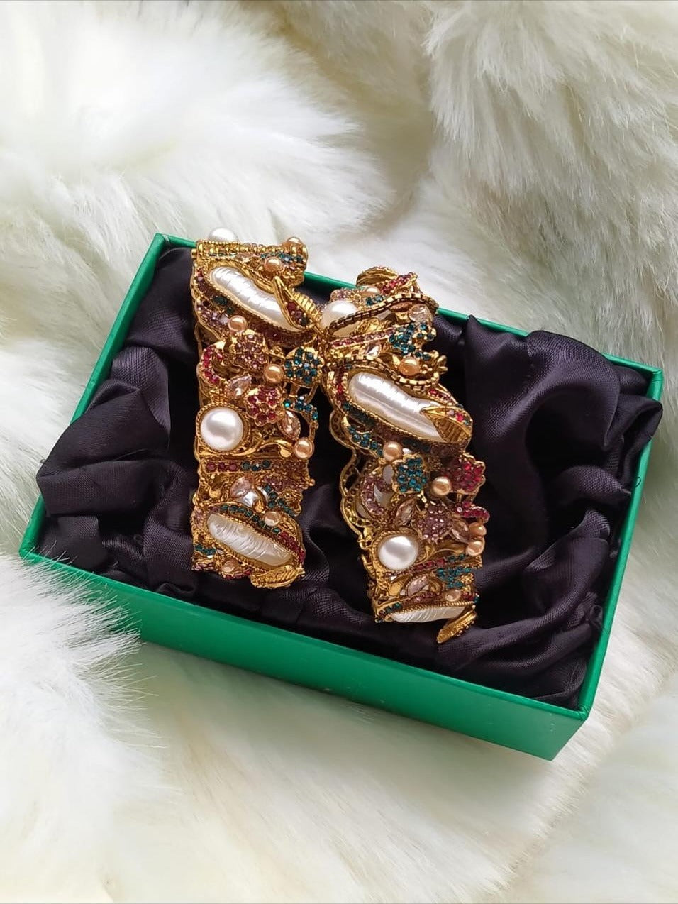 Decorative bow with pearls and gemstones in a green box on a white fur background