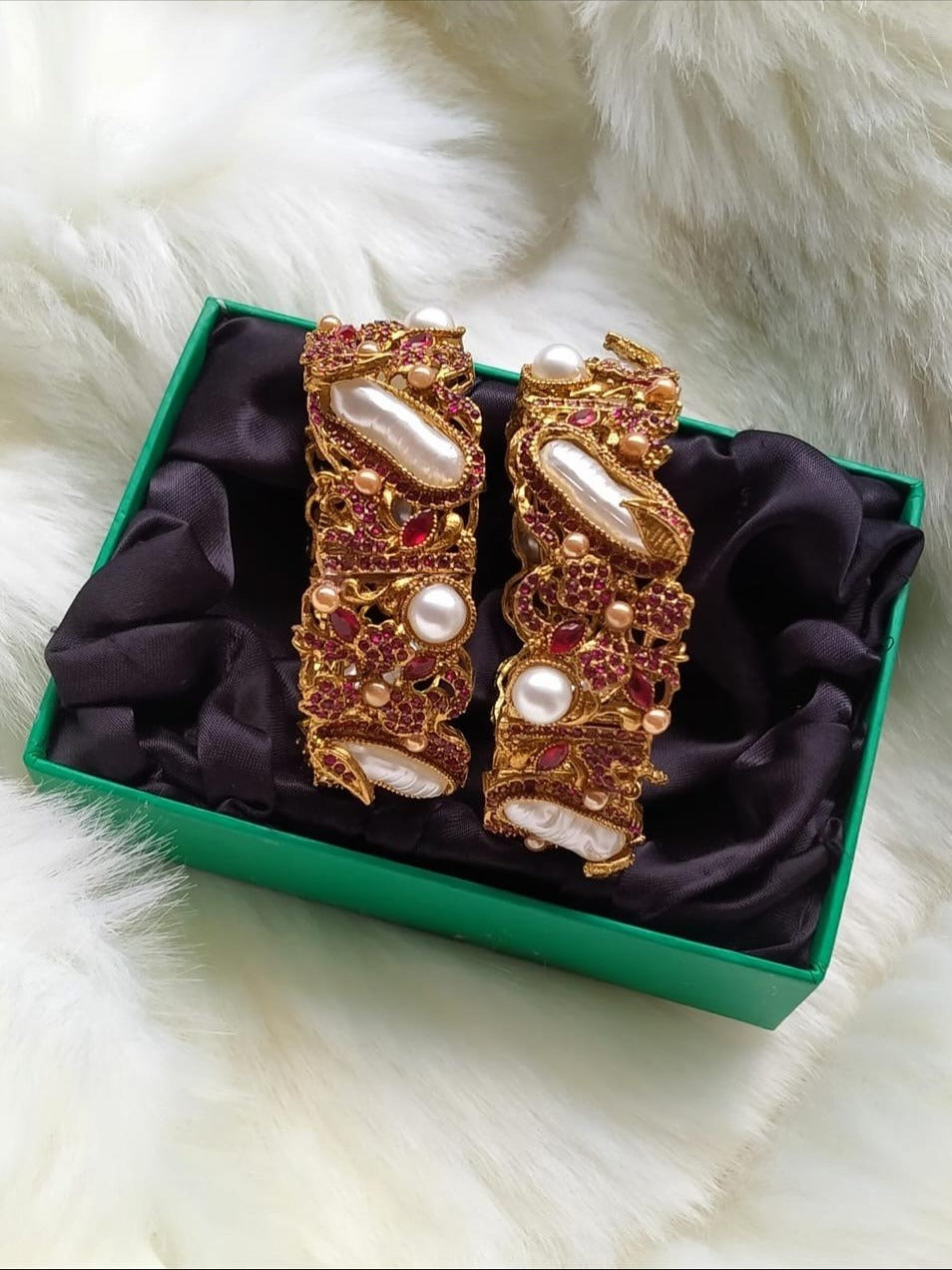 Decorative bracelets with pearls and gemstones in a green box on a fluffy white surface